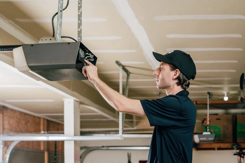 Technician fine-tuning a garage door opener after install — final QC check